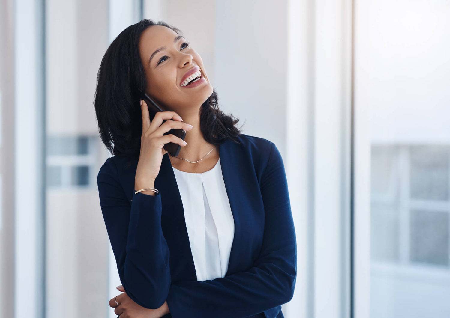 Confident entrepreneur in a navy blazer smiling while talking on the phone in a modern office space with natural light, representing success and professionalism in the MRR and PLR digital product business.